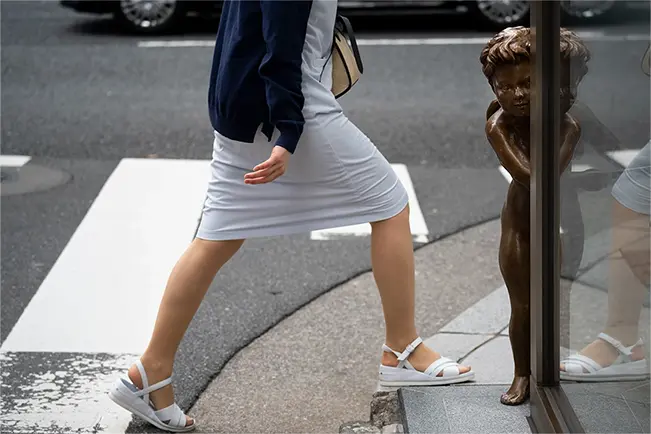 Woman walking past a bronze statue on a city street