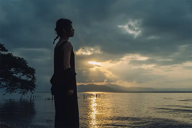 Woman standing beside a lake at sunset under a dramatic cloudy sky