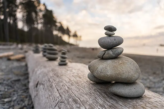 Stacked smooth stones arranged on a weathered log beside the beach