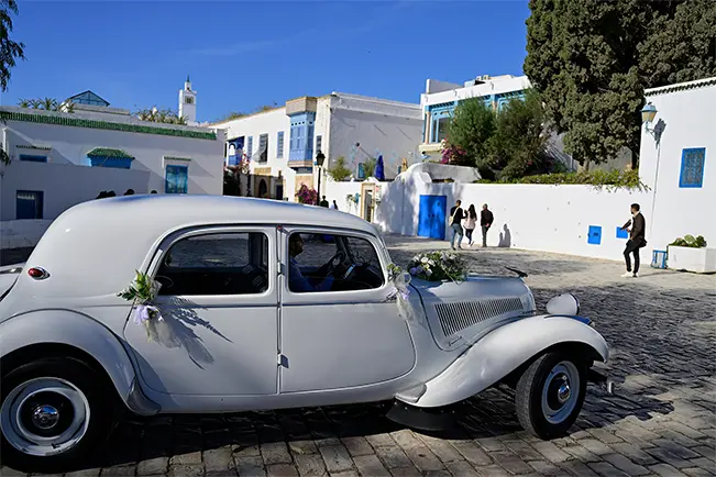 Vintage white car parked on a sunny street lined with white buildings