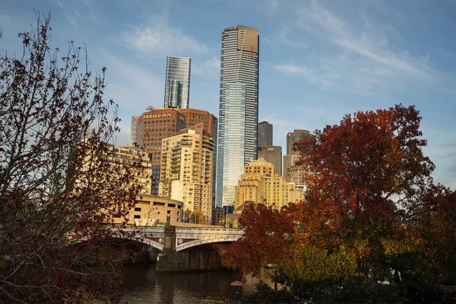 City skyline with tall buildings, autumn trees, and a river